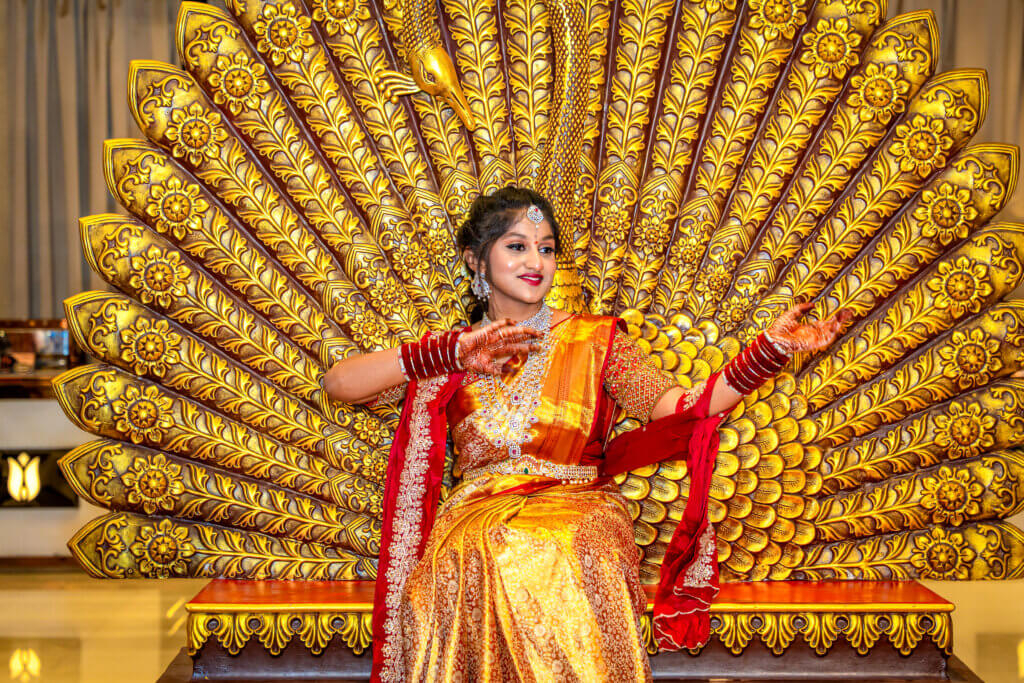 Girl in a gold saree sitting on a chair and joyfully dancing during her saree ceremony.