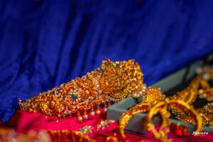 Close-up of a traditional gold vaddanam (waist belt) adorned with intricate designs and gemstones, worn over a silk saree by a young girl during her saree ceremony.